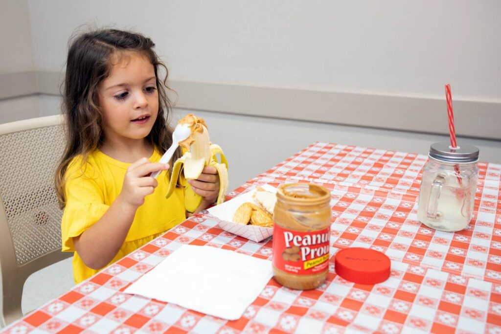 Niña comiendo mantequilla de maní. Una niña poniéndole mantequilla de maní a una banana.
Fotografía cortesía de UF/IFAS.